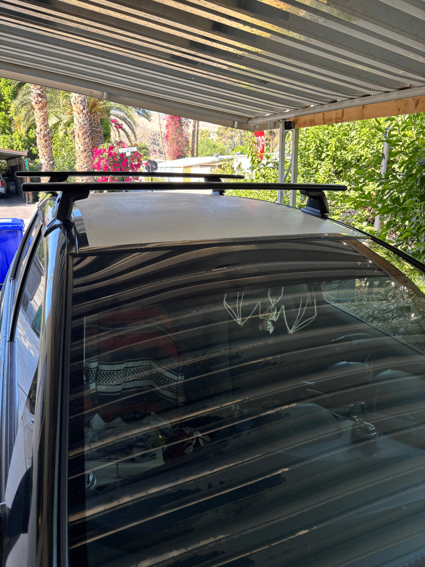 A car parked under a carport, its roof coated with CryoPaint, framed by palm trees and bright bougainvillea in the Cathedral City desert.