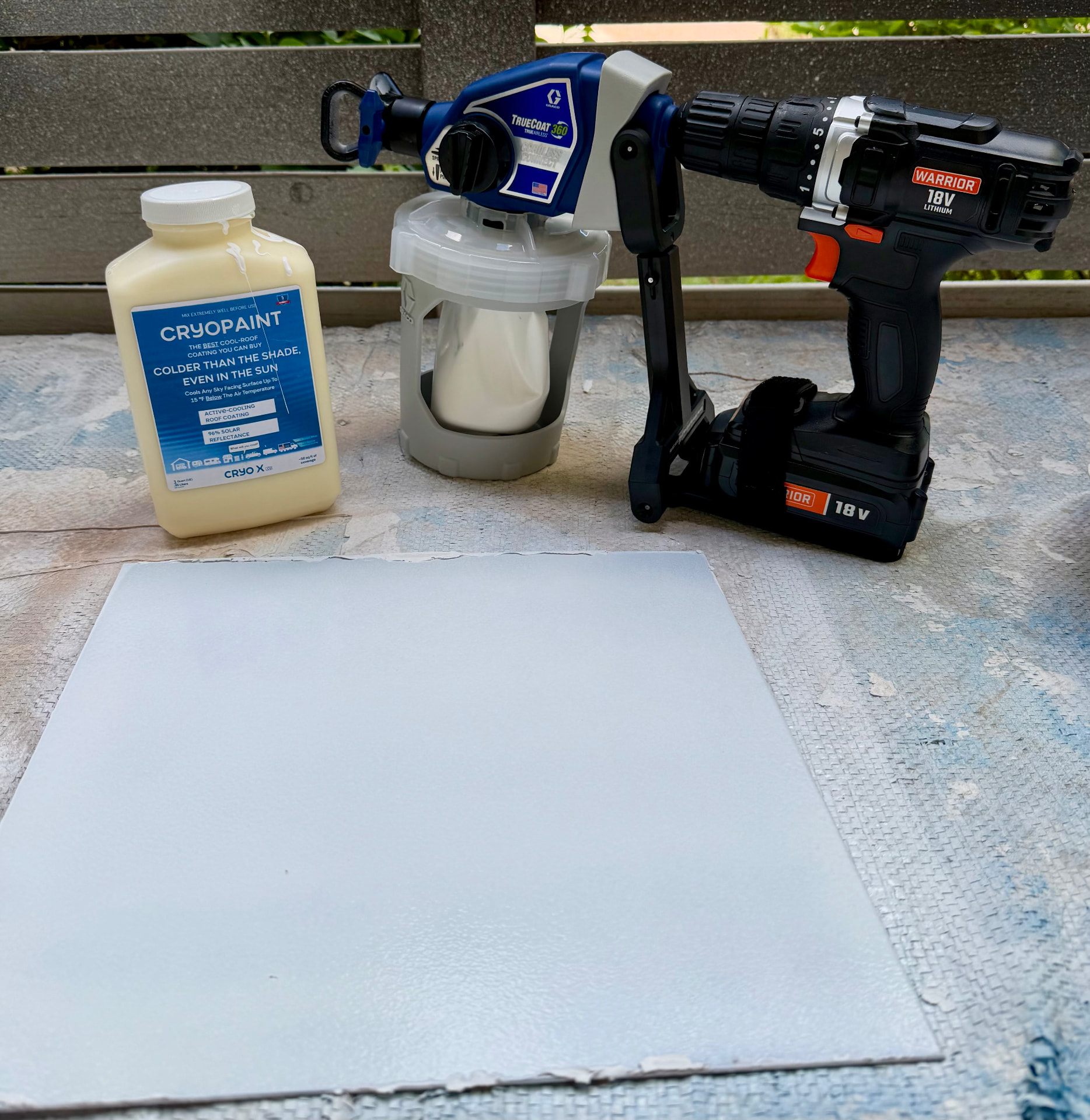Graco TrueCoat 360 handheld cordless drill paint sprayer next to a quart of CryoPaint and a freshly sprayed white panel